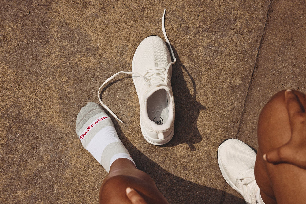A close-up of a foot wearing a Swiftwick sock next to a sneaker on a concrete surface.