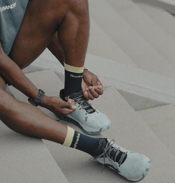 Athlete sitting on steps, tying shoes while wearing black and yellow Swiftwick socks.