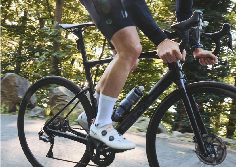 Cyclist in black gear riding on a forest road with a water bottle