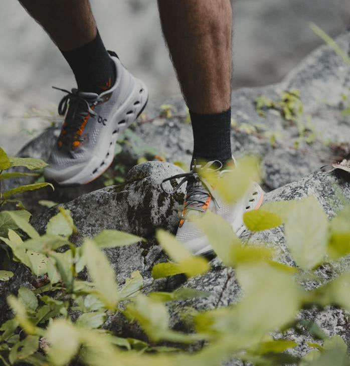 Person hiking on rocks outdoors wearing gray shoes and black Swiftwick socks.