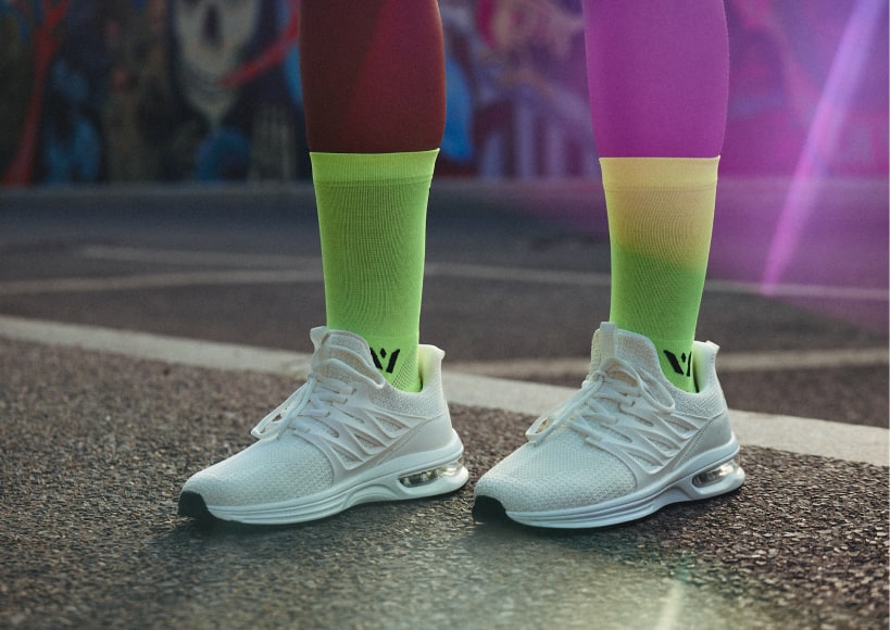 Closeup of a runner wearing Swiftwick yellow socks and white running shoes on pavement.