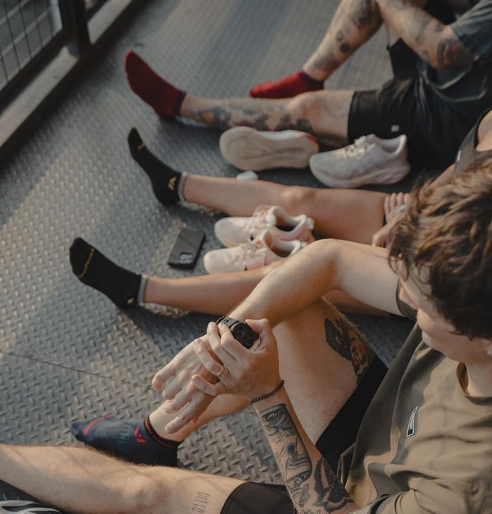 Group of people sitting on a metal floor with shoes off, showing colorful Swiftwick socks.