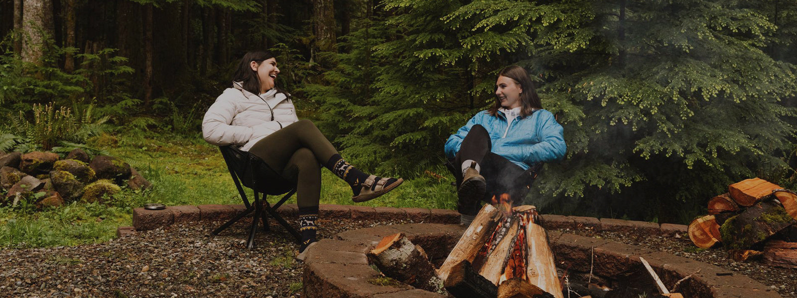 Two women sitting by campfire wearing Swiftwick socks