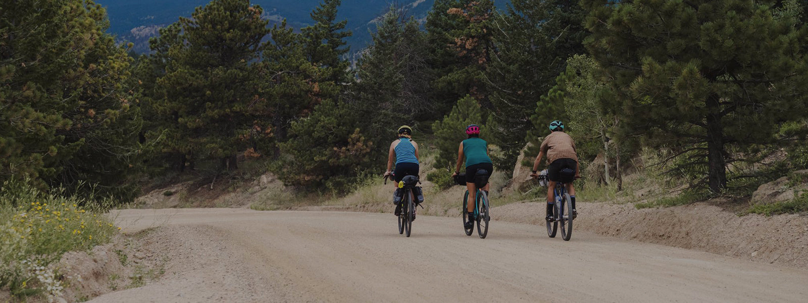 Three people cycling down dirt road