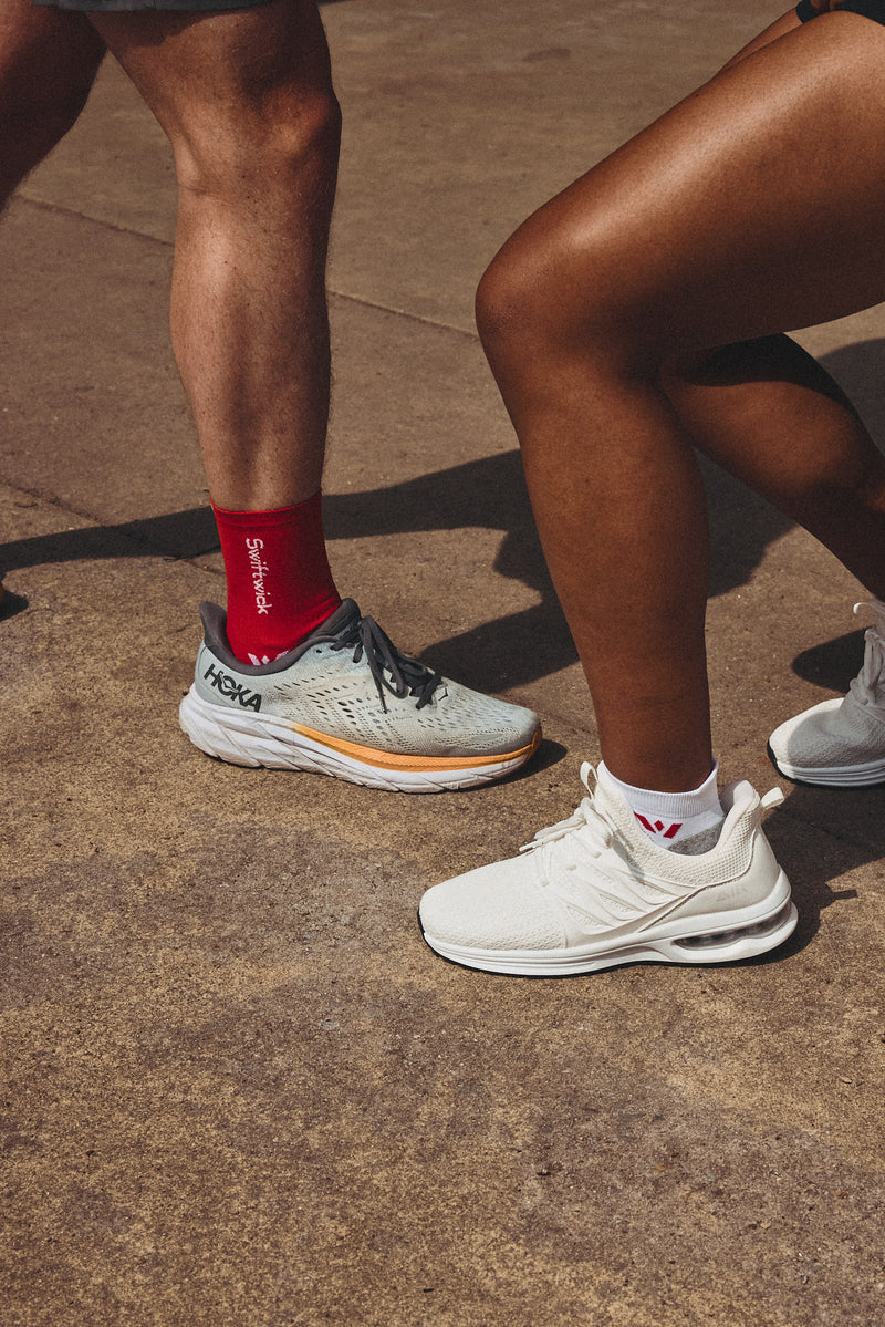 Closeup of two runners wearing Swiftwick socks and running shoes on pavement.