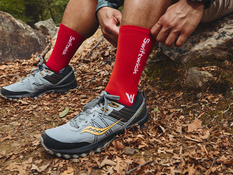 Hiker pulling up their Endurance Red Swiftwick socks on forest trail.