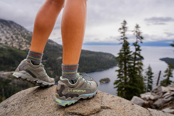 Closeup of hiker in Swiftwick socks and hiking shoes overlooking a lake and shoreline.