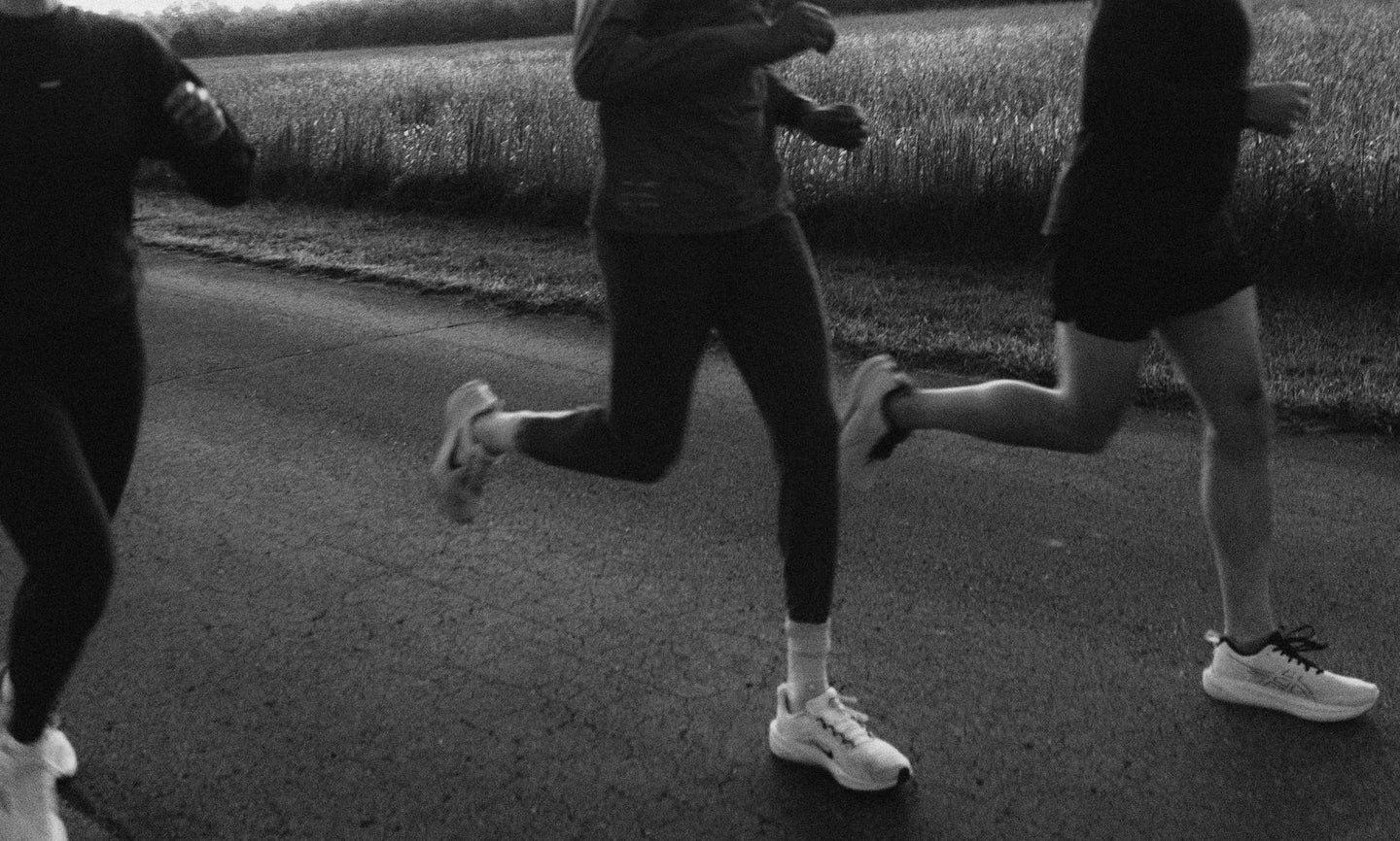 Black-and-white image of three runners on an outdoor track, mid-stride, showing their legs and torsos.