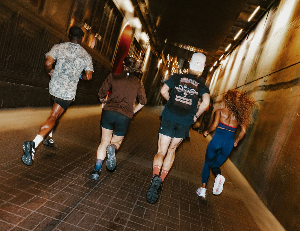 Group of runners in athletic apparel running through a dim urban tunnel