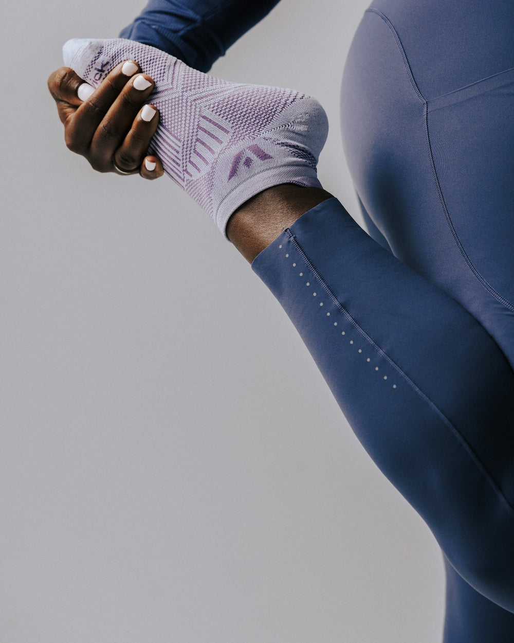 Hands pulling on a lavender Aspire No Show sock at the ankle
