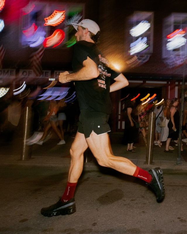 Runner at night on a lit city street in a green top and black shorts