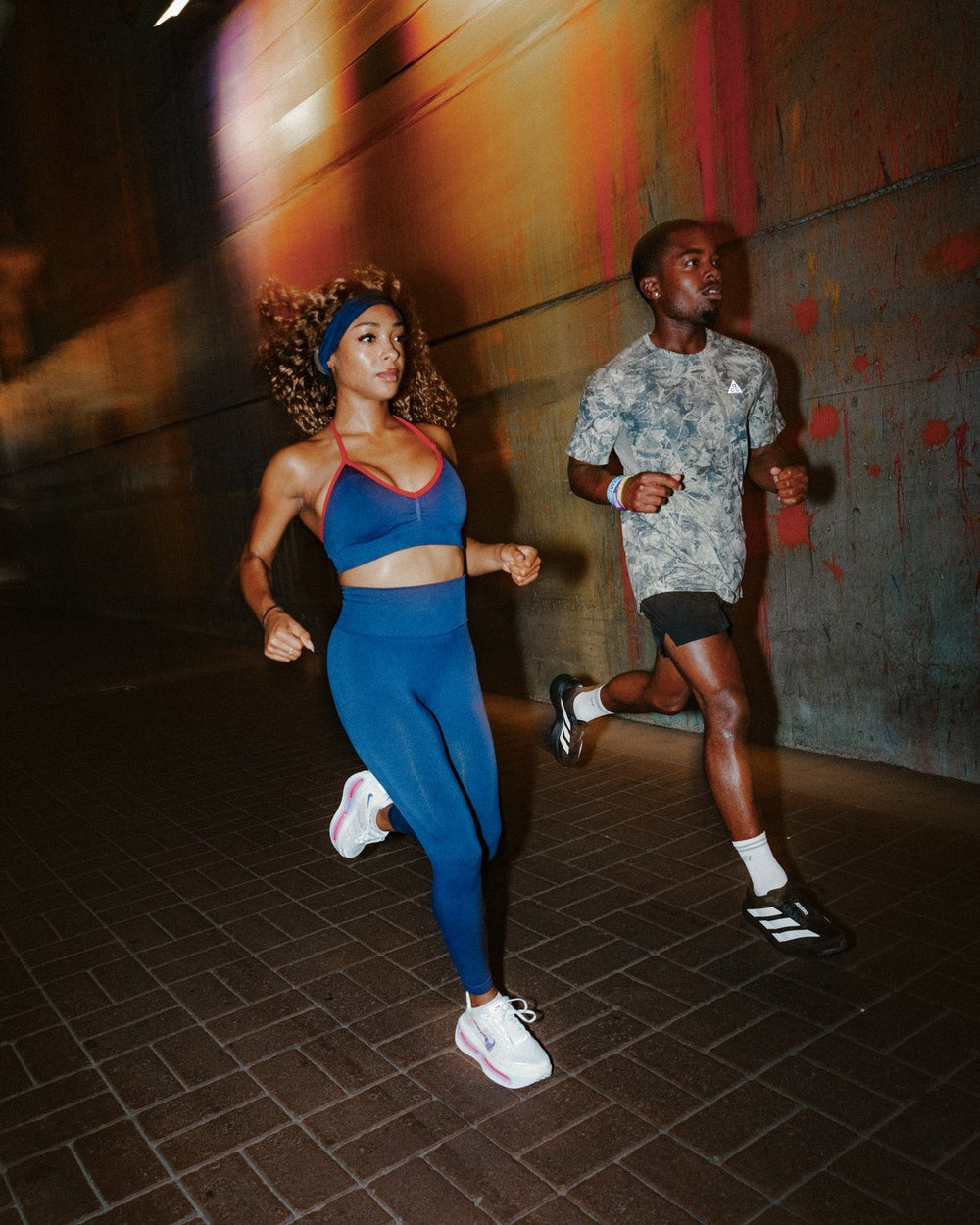 A man and woman running at night in a city in teal gear and white Maxus Mid-Crew socks