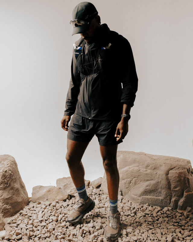 Man walking on rocky terrain outdoors in a gray jacket and navy Pursuit Crew socks