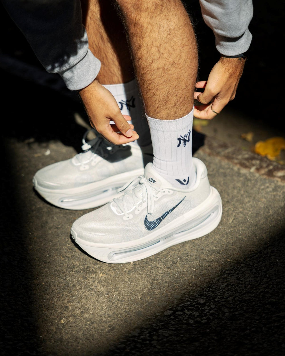 Closeup of a persons feet in white NY socks and white Nike sneakers on pavement